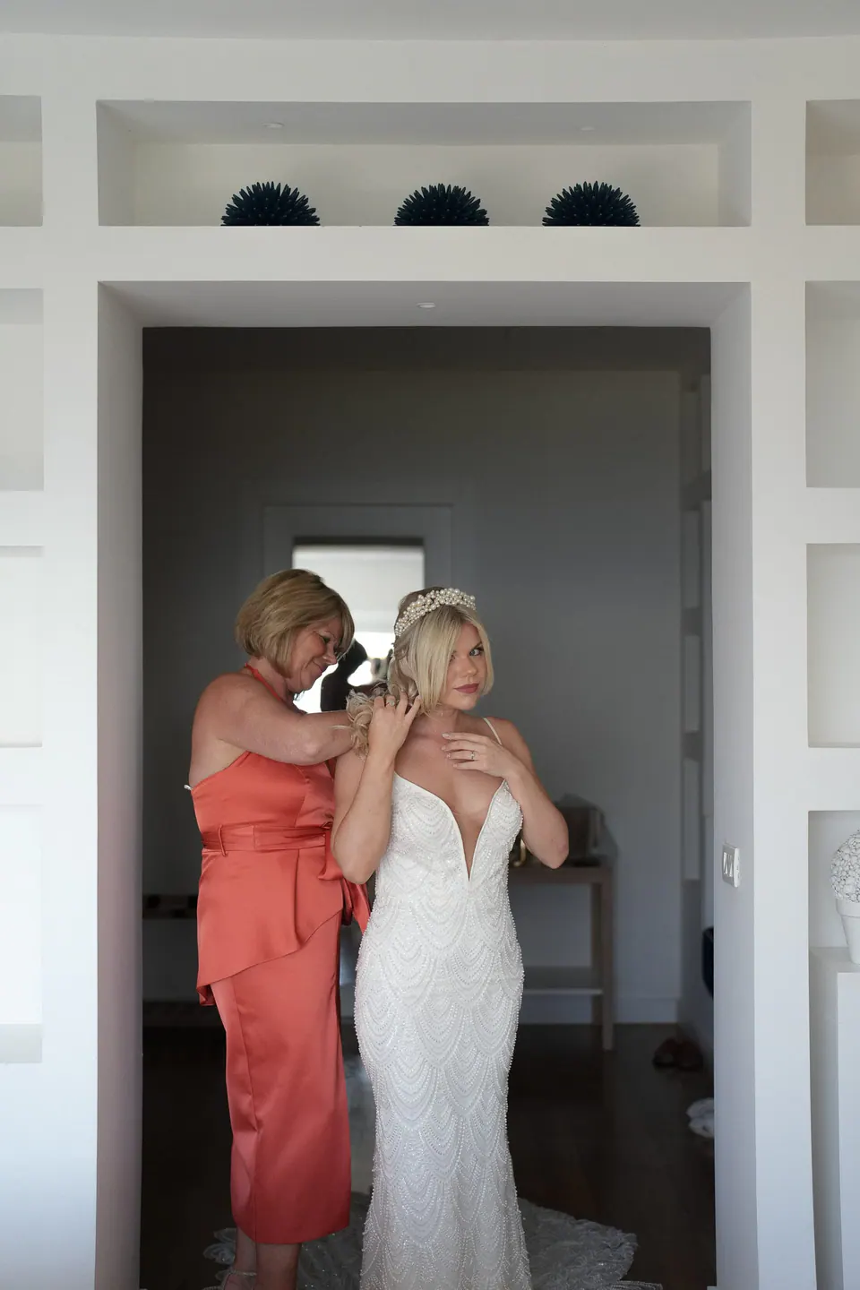 Bride hugging a guest in coral in a white doorway