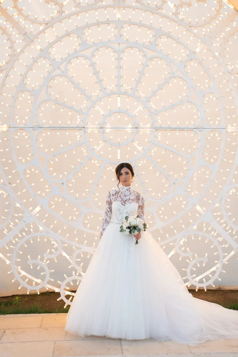 Bride standing in front of the illuminated carved stone arch