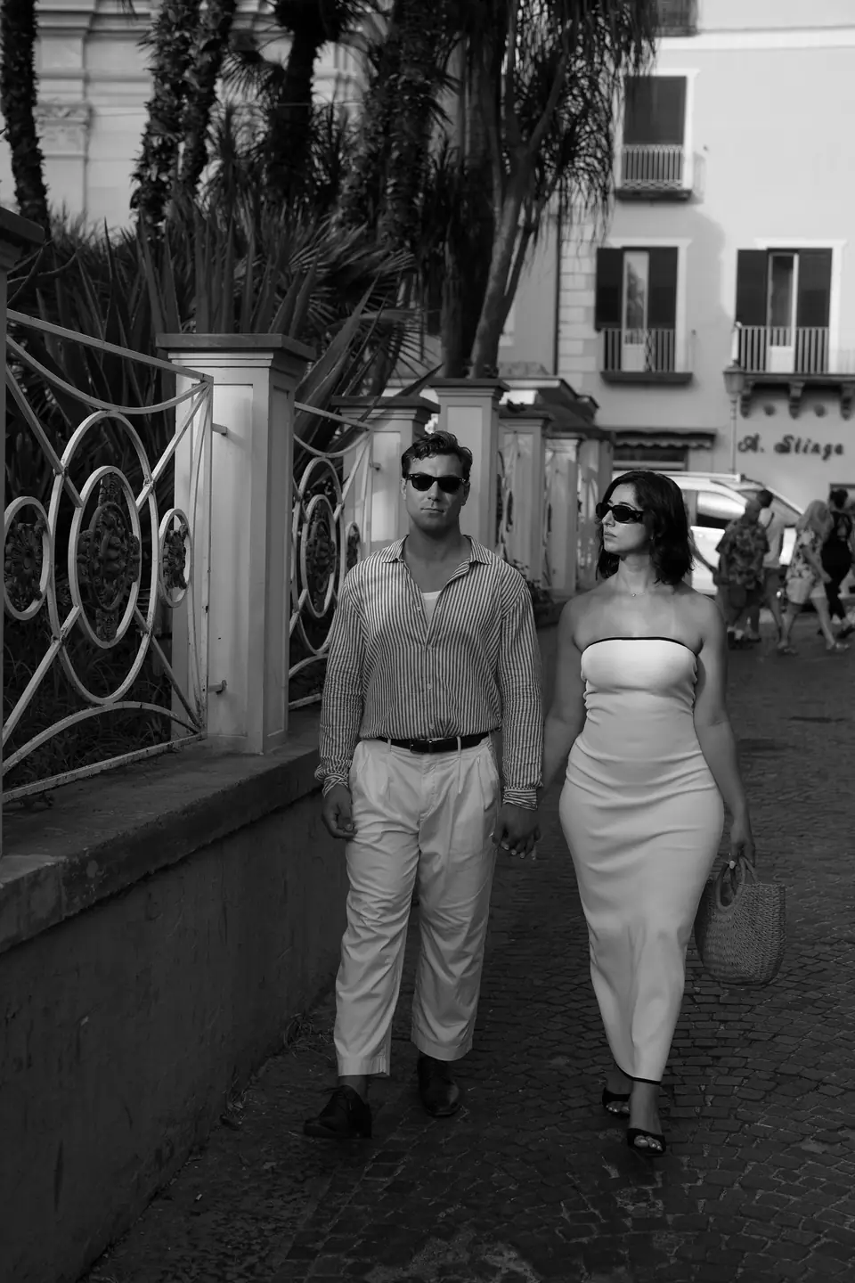 Black and white photo of the couple walking past a wrought-iron gate.