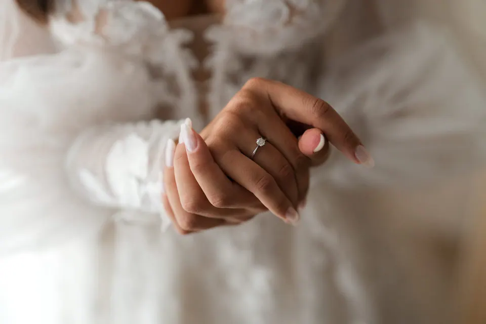 Close-up of the bride's hands and engagement ring against the lace of her gown.