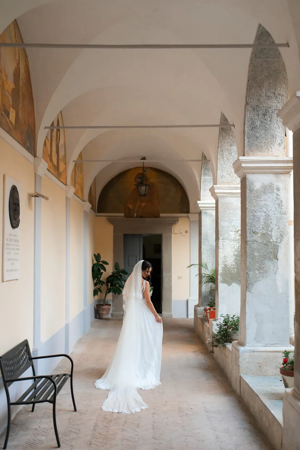 Bride walking along the arcaded cloister of Villa Angelina, her veil trailing.