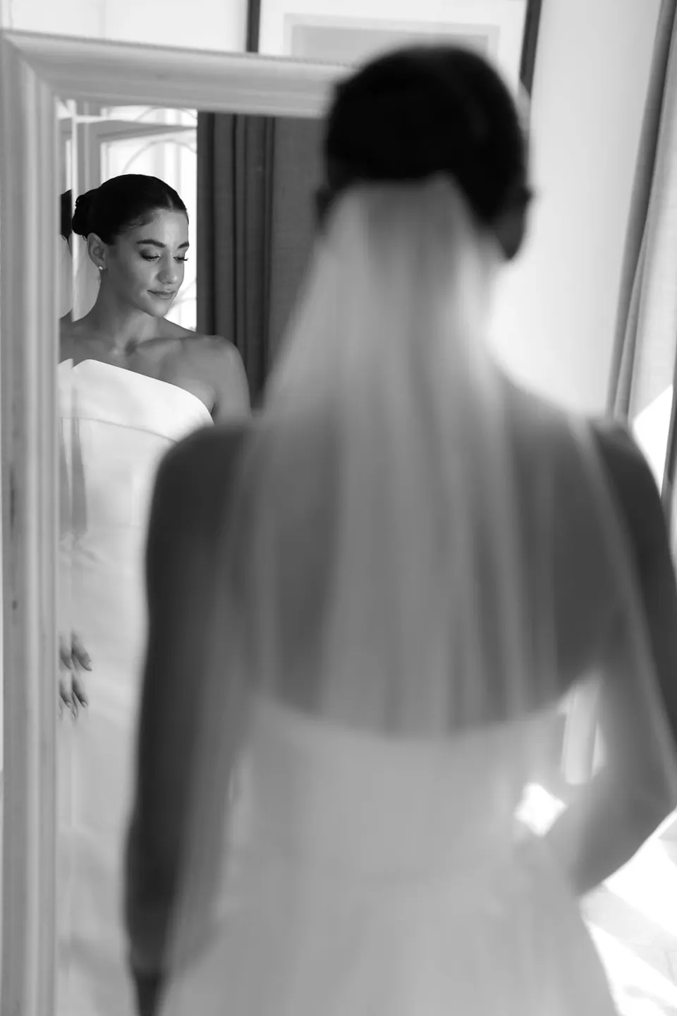 Black and white photo of the bride in her veil reflected in a mirror.