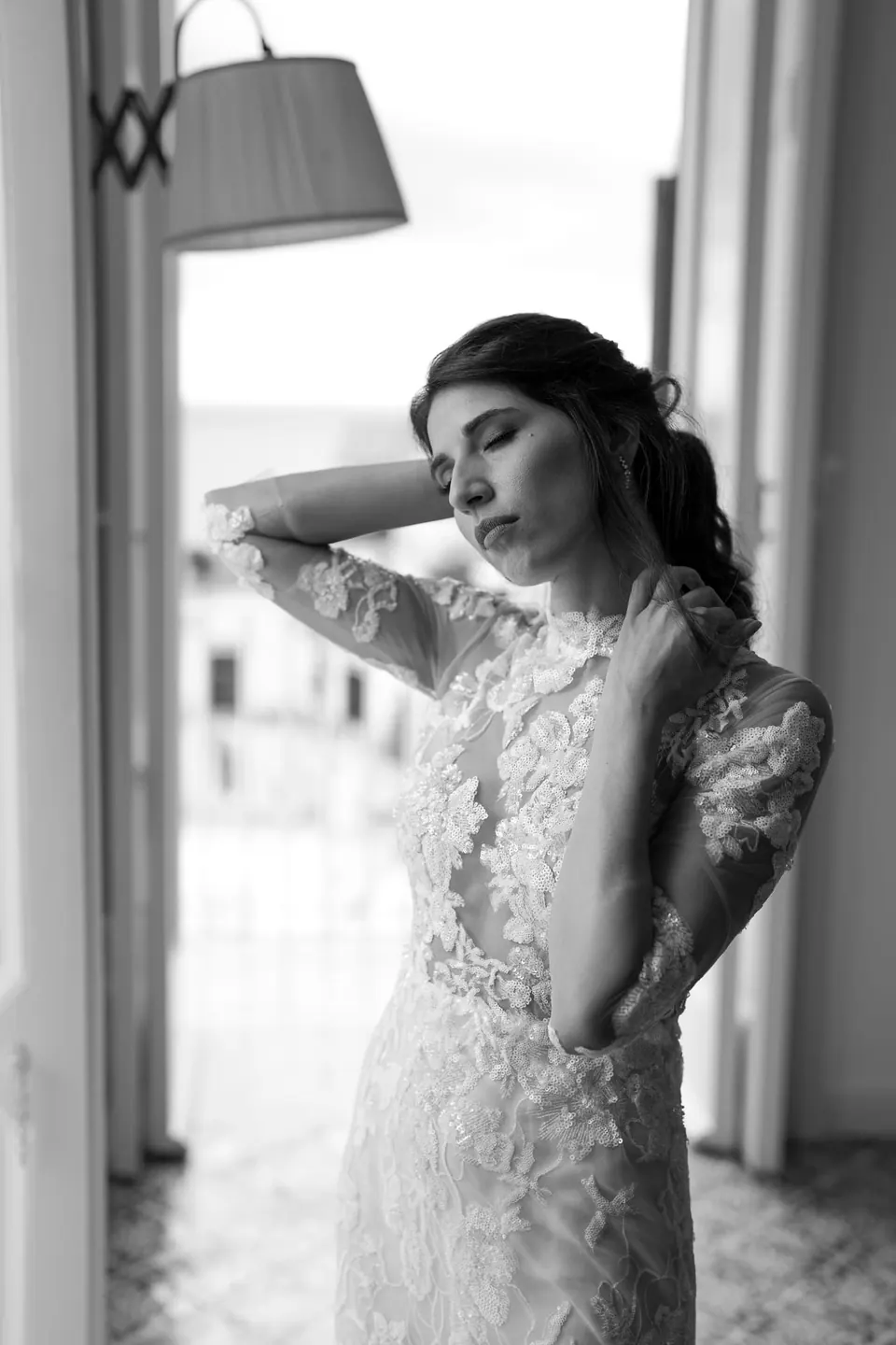 Die Braut im Spitzenkleid blickt in weichem Licht in die Ferne.