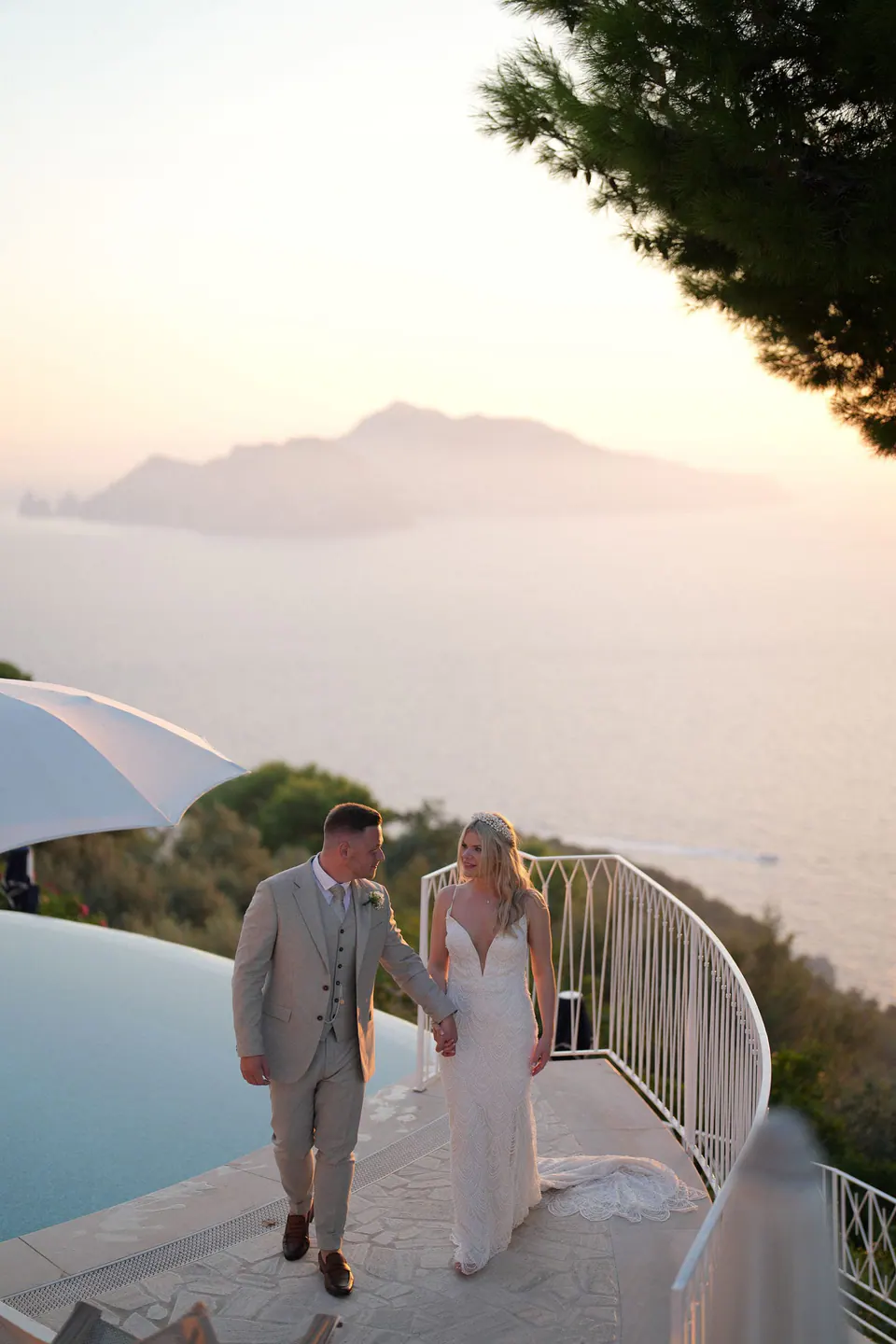 Sposi che camminano accanto alla piscina con Capri all'orizzonte al tramonto
