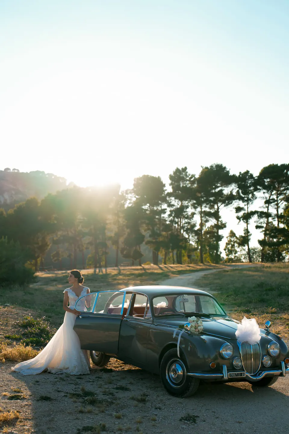 Bride and groom with a vintage car in a pine grove at sunset