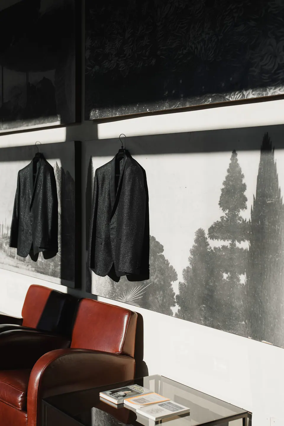 Zwei Sakkos am Fenster über einem roten Ledersessel.