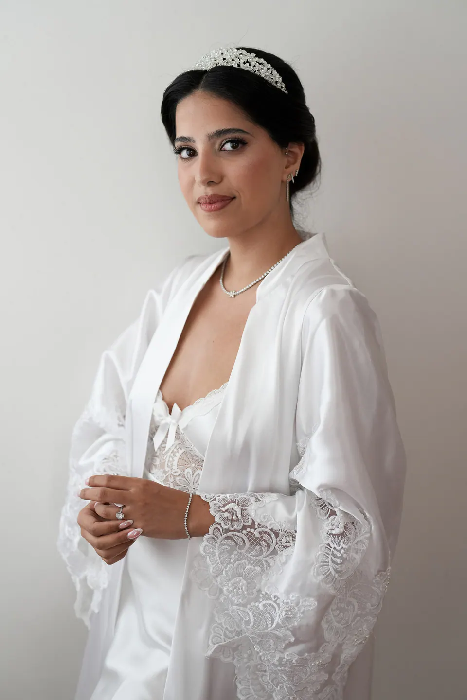 Portrait de la mariée en peignoir qui regarde par-dessus son épaule, un collier fin au cou.