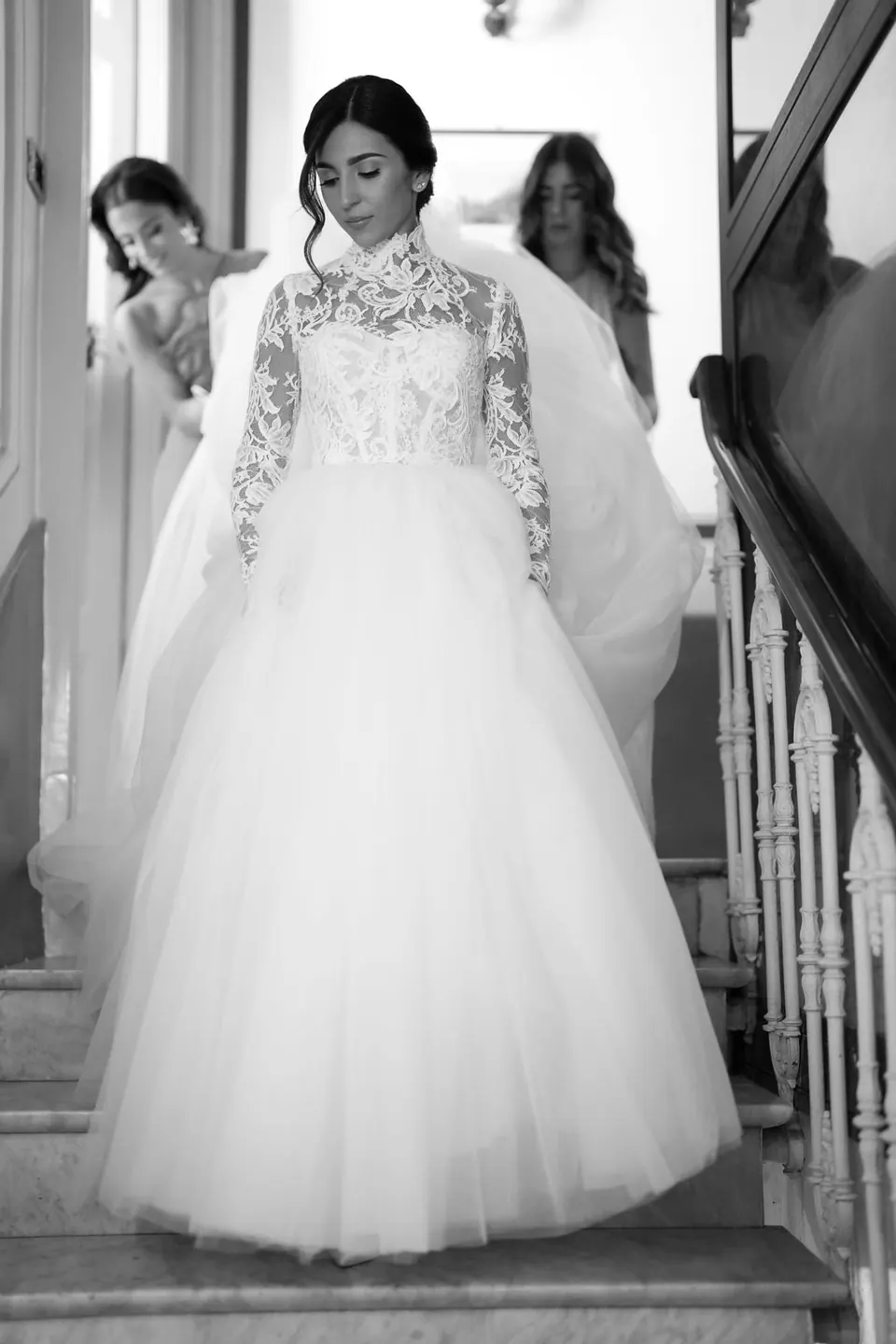 Black and white photo of the bride coming down the stairs with the women of the family