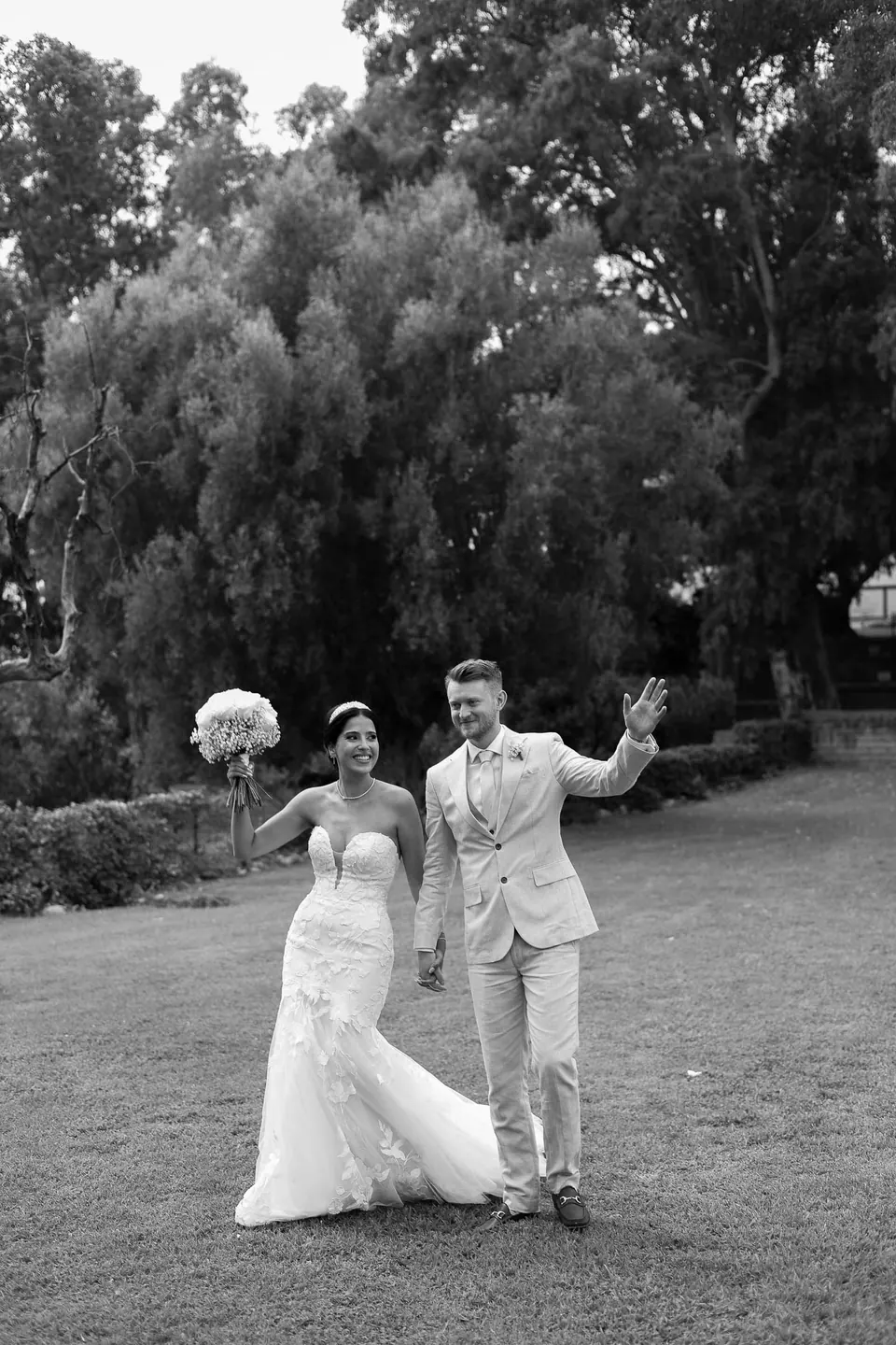 Les mariés traversent la pelouse en noir et blanc, elle lève son bouquet, il fait signe de la main.