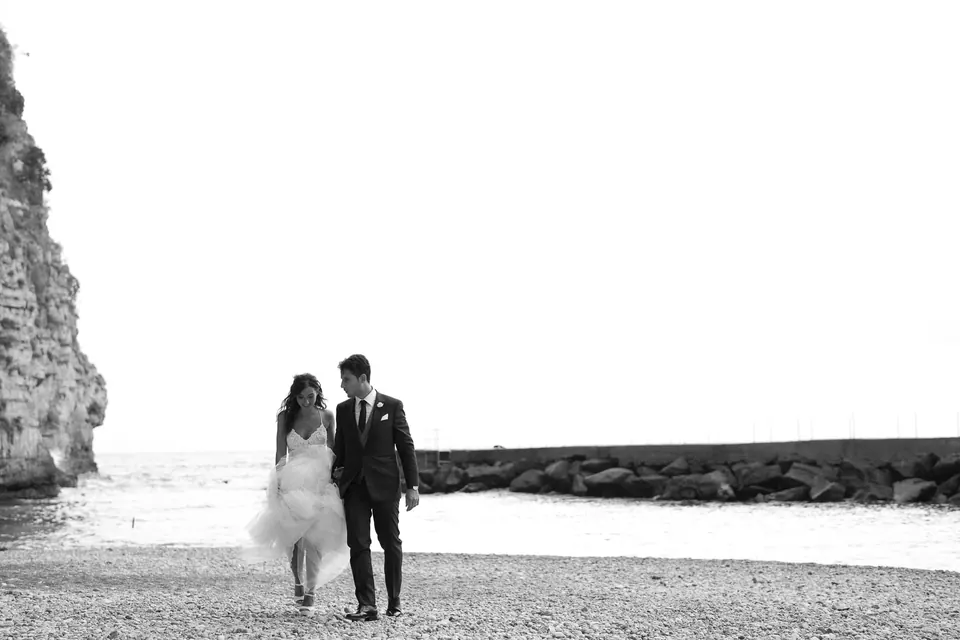 Foto in bianco e nero degli sposi che camminano sulla spiaggia sotto Vico Equense.