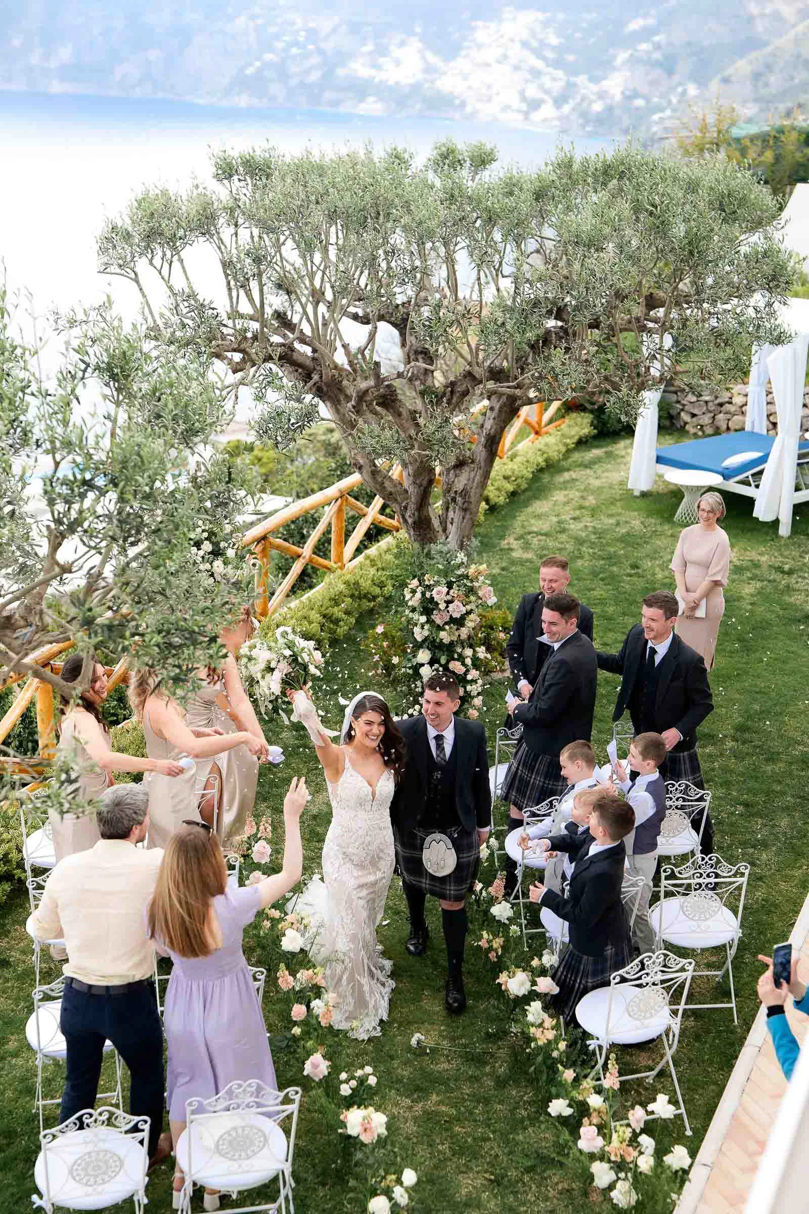 Newlyweds walking back up the aisle among guests on the lawn of Villa Milù, seen from above.
