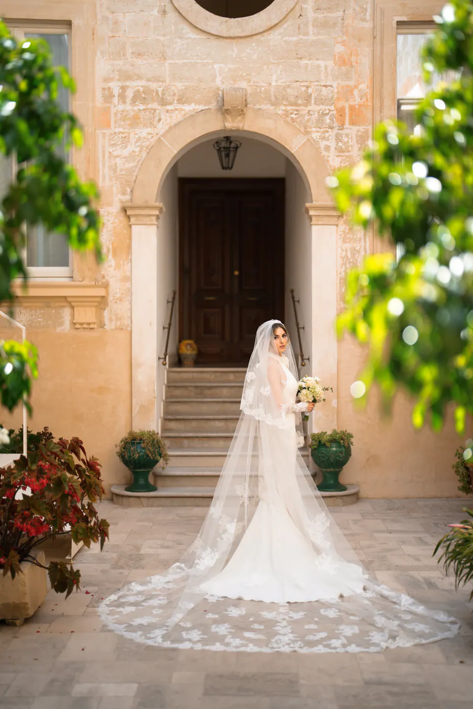 La sposa in un cortile di pietra, con il velo lunghissimo aperto sul selciato.