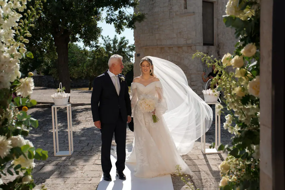 La novia entra con su padre entre ramos de flores blancas.