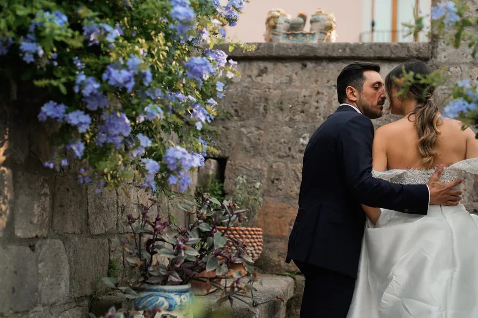 Groom kissing the bride under a wall of blue flowers