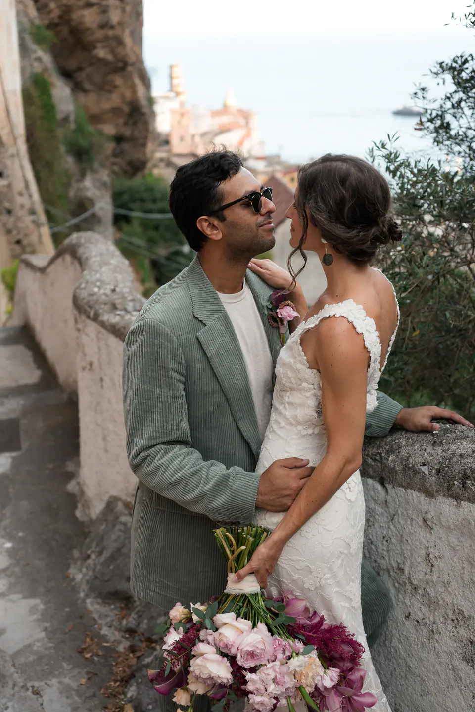 Groom kissing the bride on a staircase, the sea and a church behind.