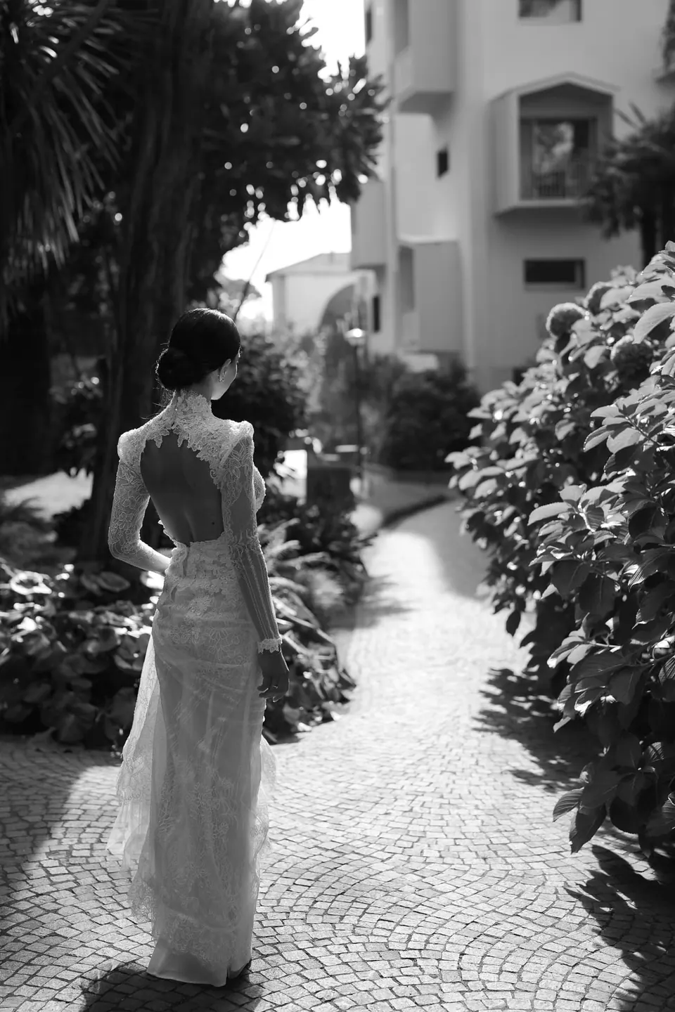 Schwarzweißfoto: Die Braut geht den Gartenweg des Hotels hinunter.
