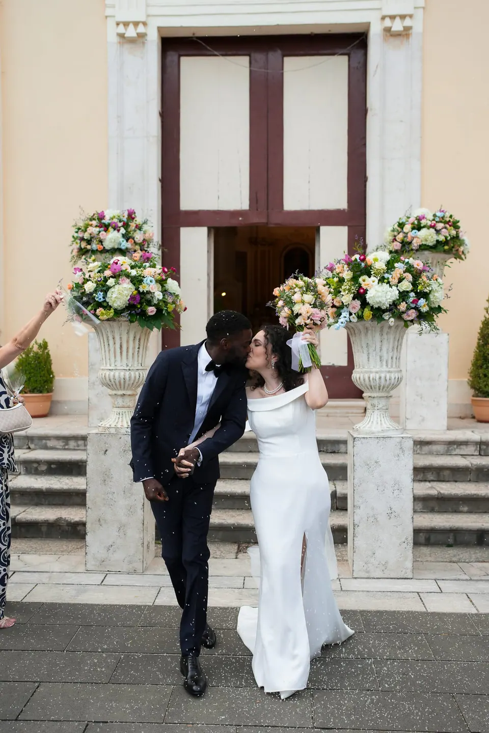 Los novios en la entrada de la villa entre jarrones de flores rosas y blancas.