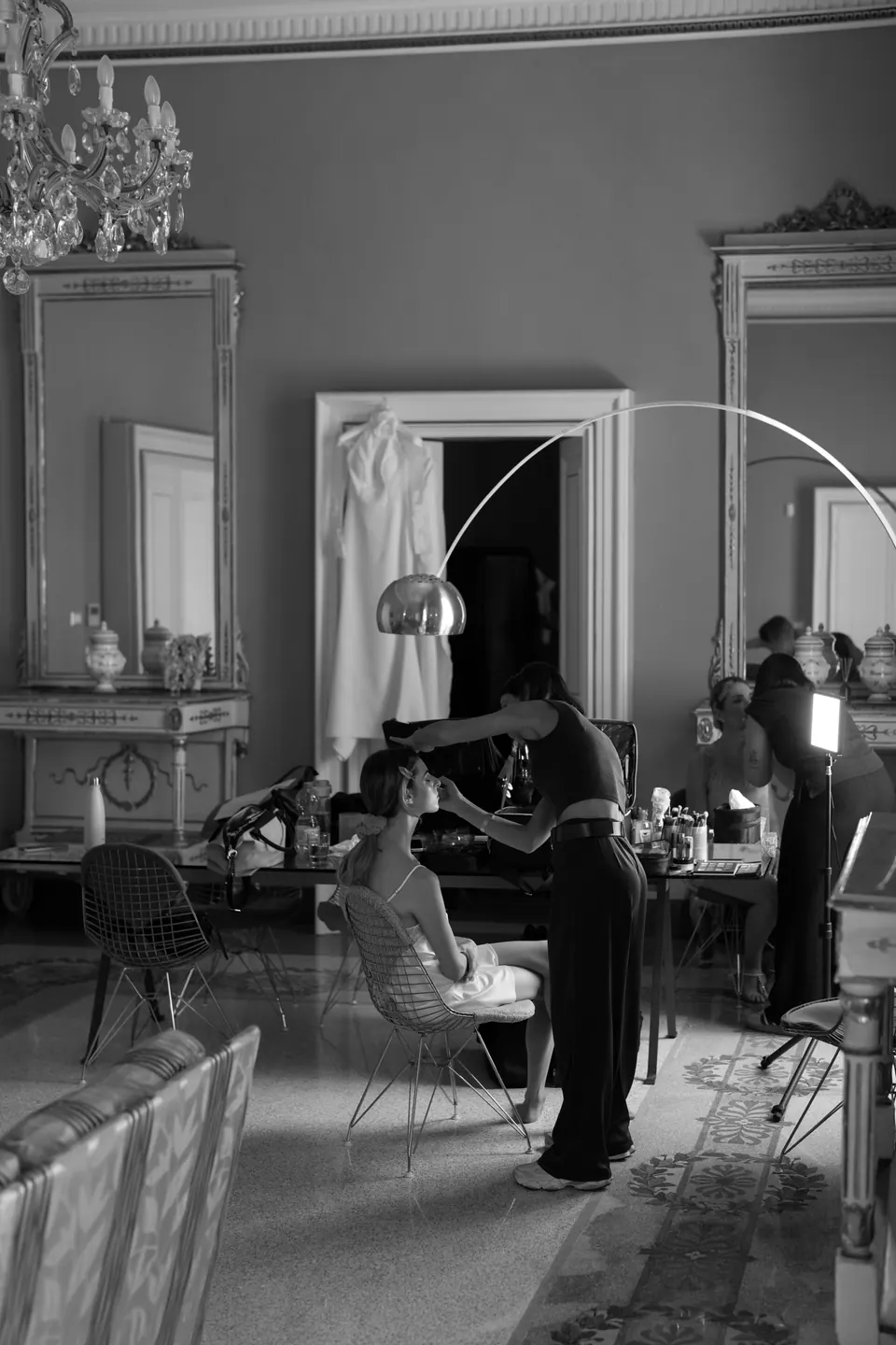 Veduta in bianco e nero della sala affrescata dove la sposa si trucca, con l'abito appeso alla porta.