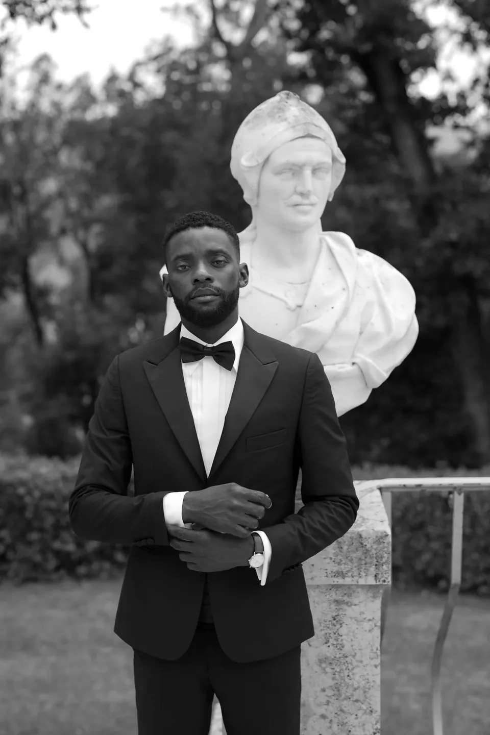 Retrato en blanco y negro del novio con esmoquin delante de un busto de mármol.