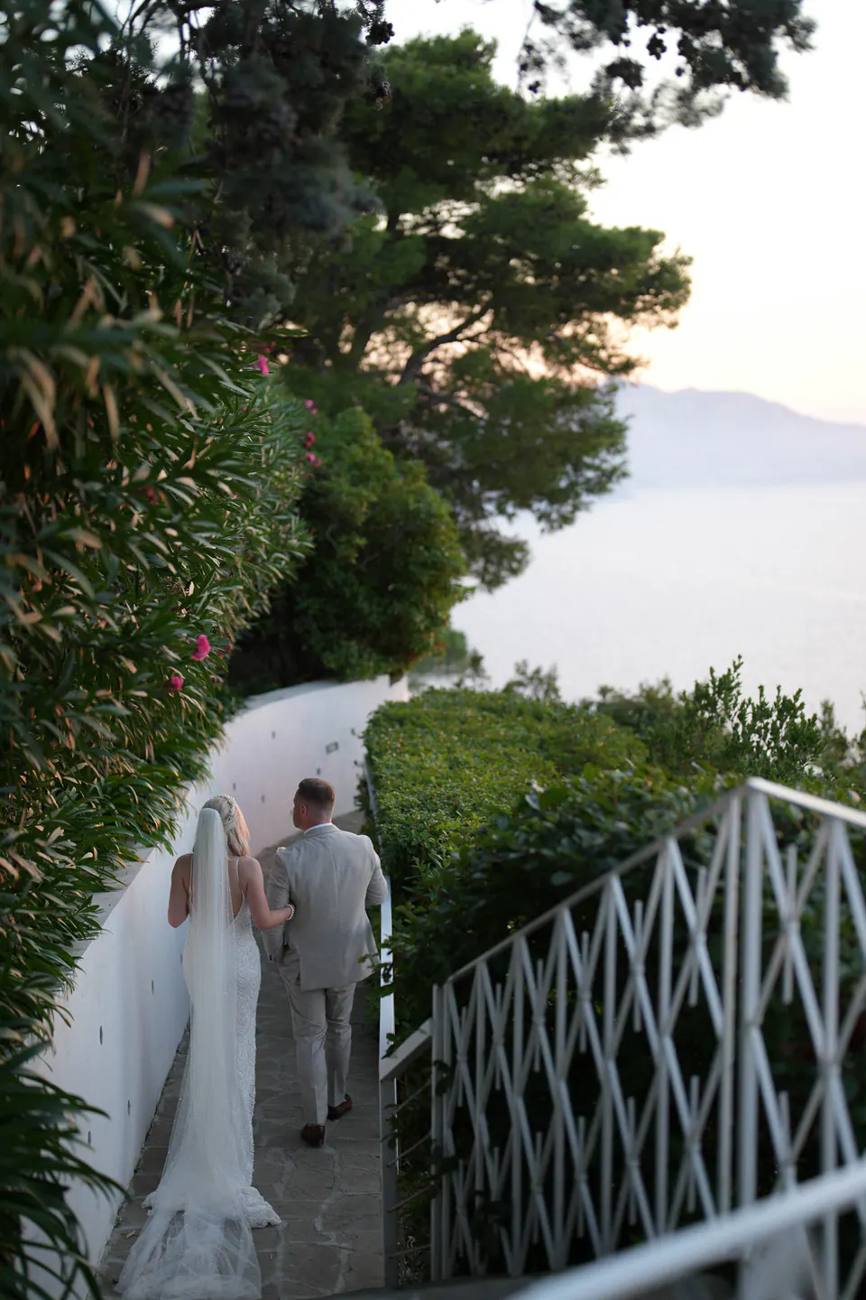 Bride and groom walking along a white railing among the trees