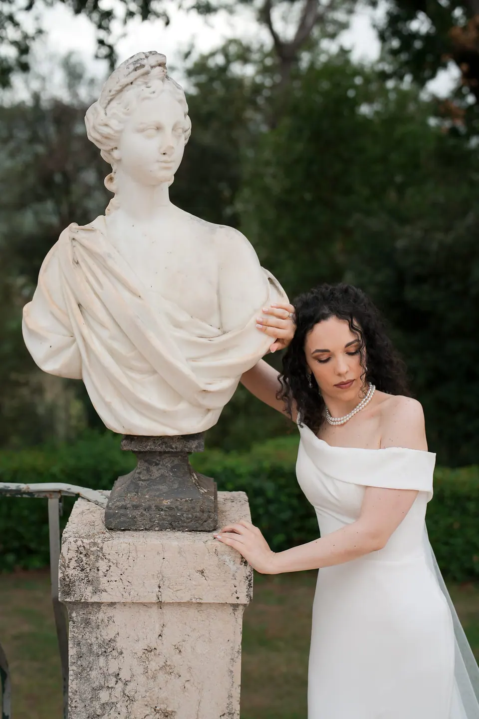 La novia ríe junto a un busto de mármol, con la mano sobre la estatua, en Villa Ortensia D’Avalos.