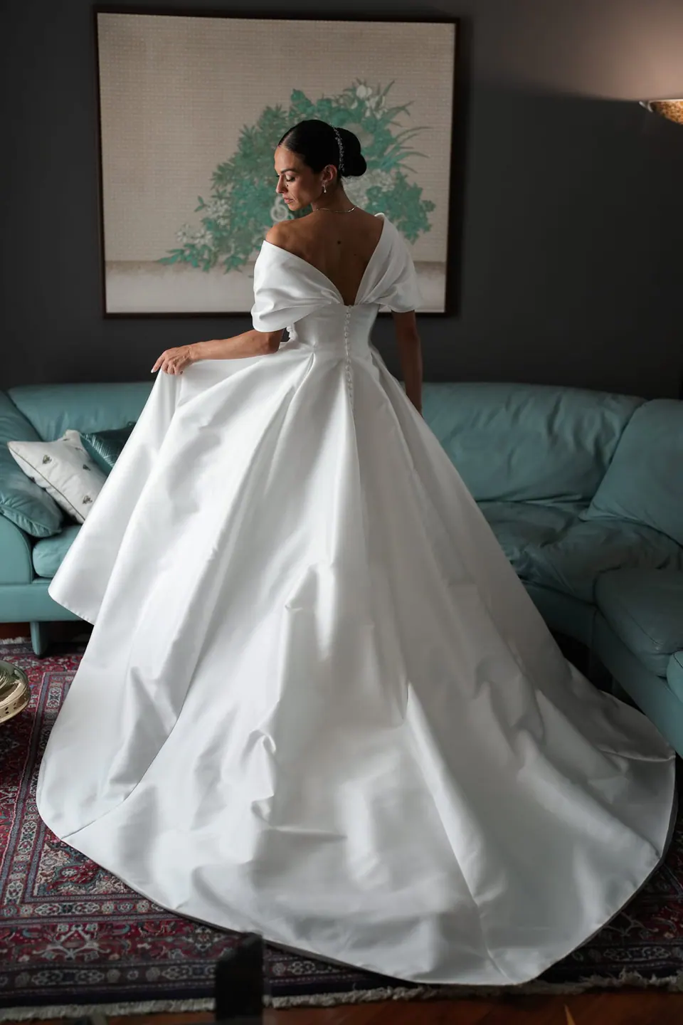 Sposa di spalle che fa volteggiare l'abito in soggiorno.