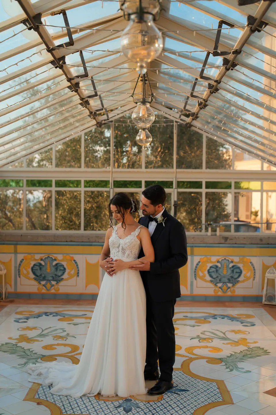 Bride and groom standing under Villa Angelina’s glass pavilion, surrounded by delicate floral arrangements.