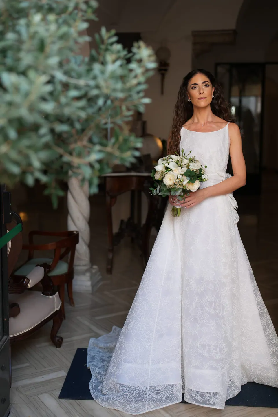 Bride standing in her lace gown with her bouquet, portrait in the hotel room.
