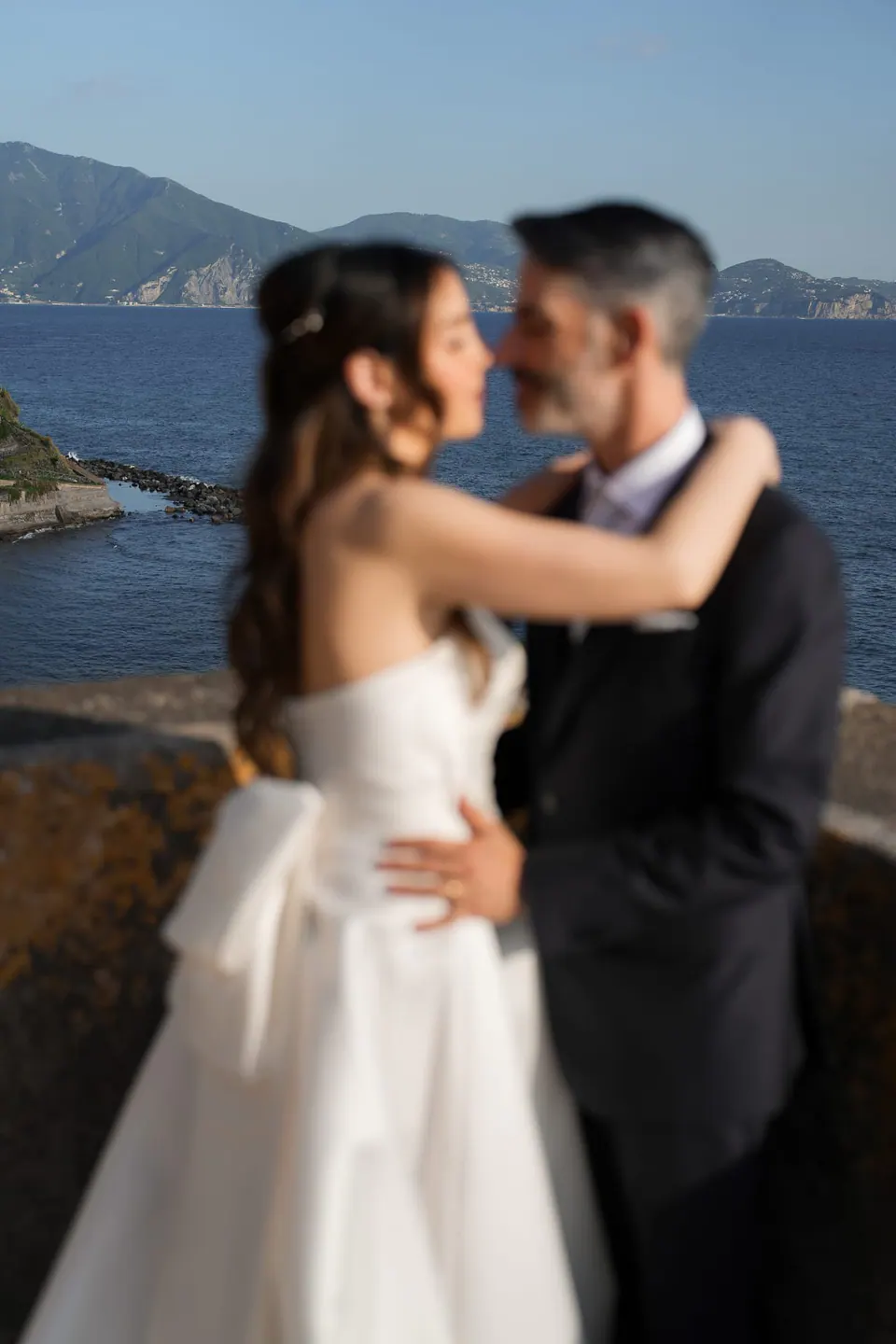 Los novios a punto de besarse, con el mar y las colinas detrás.