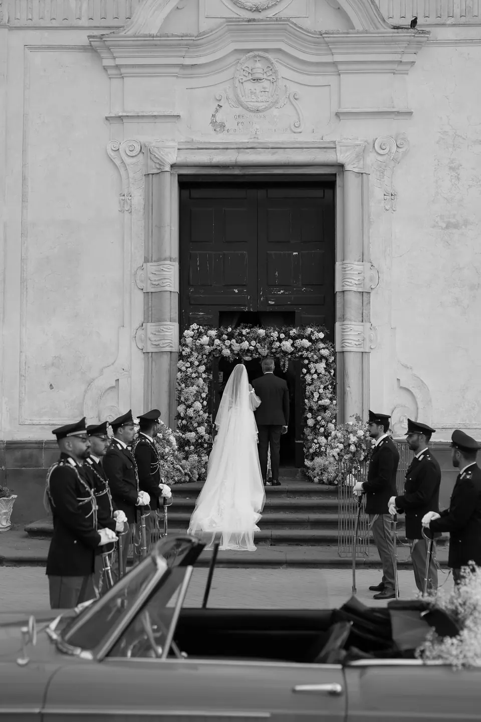 Black and white photo of the bride arriving at the church between a guard of honour in uniform.