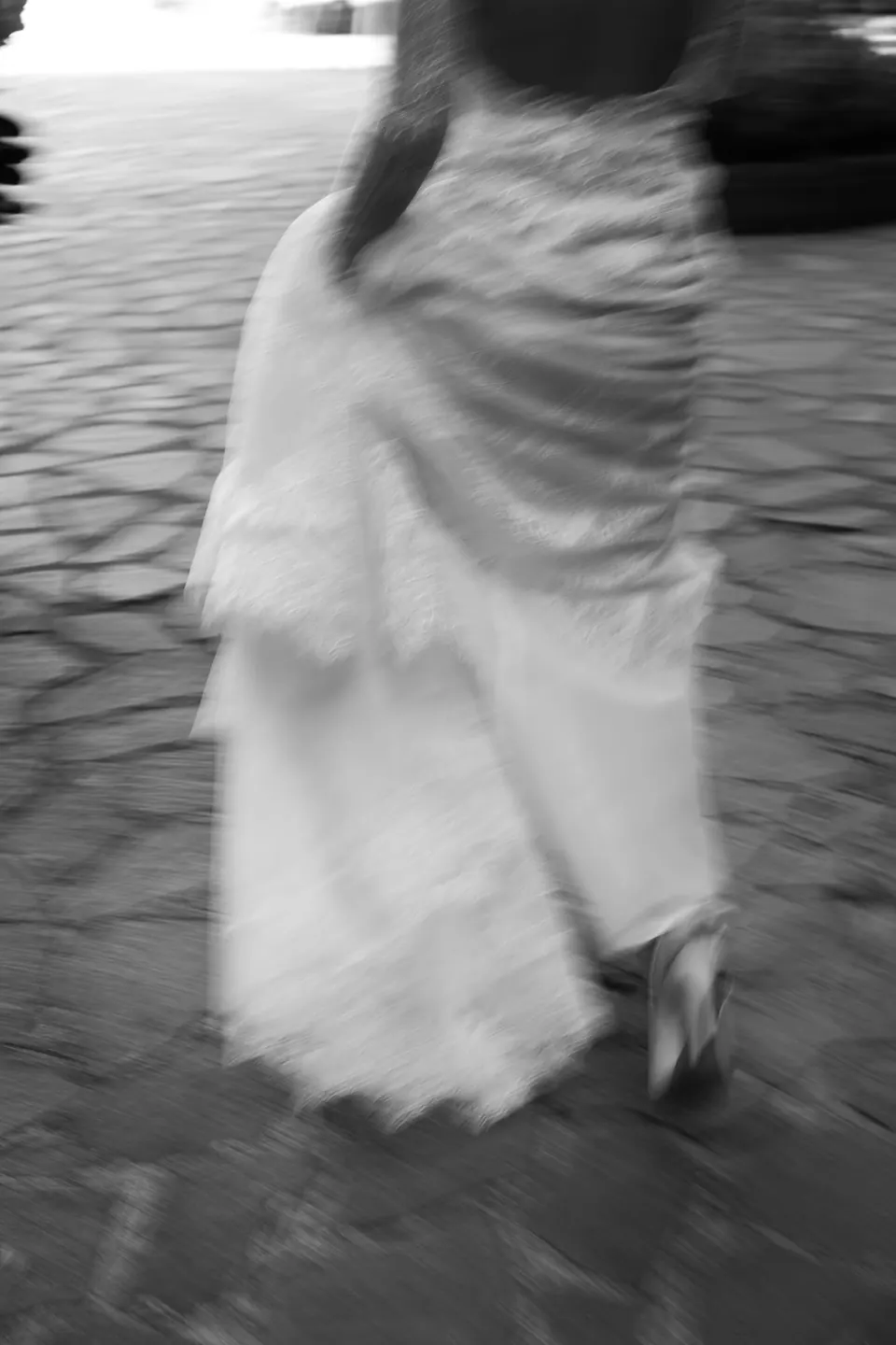 Schwarzweißfoto: Das Kleid der Braut in Bewegung auf dem Pflaster.