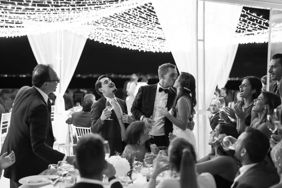 Foto in bianco e nero degli invitati che festeggiano a cena sotto le lucine.