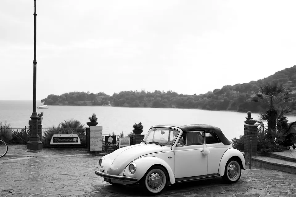 Weißes Käfer-Cabrio an der Uferpromenade, dahinter die Küste von Castellabate.