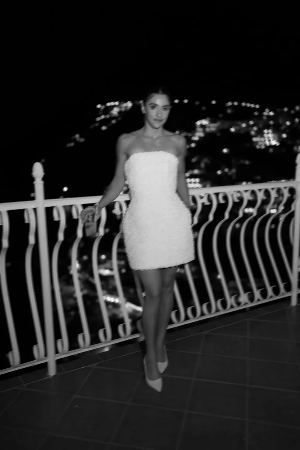 Black and white photo of the bride in a short white dress on the terrace at night.