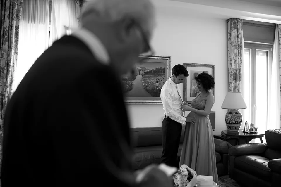 Black and white photo of an older man in the foreground as the bride gets ready behind him