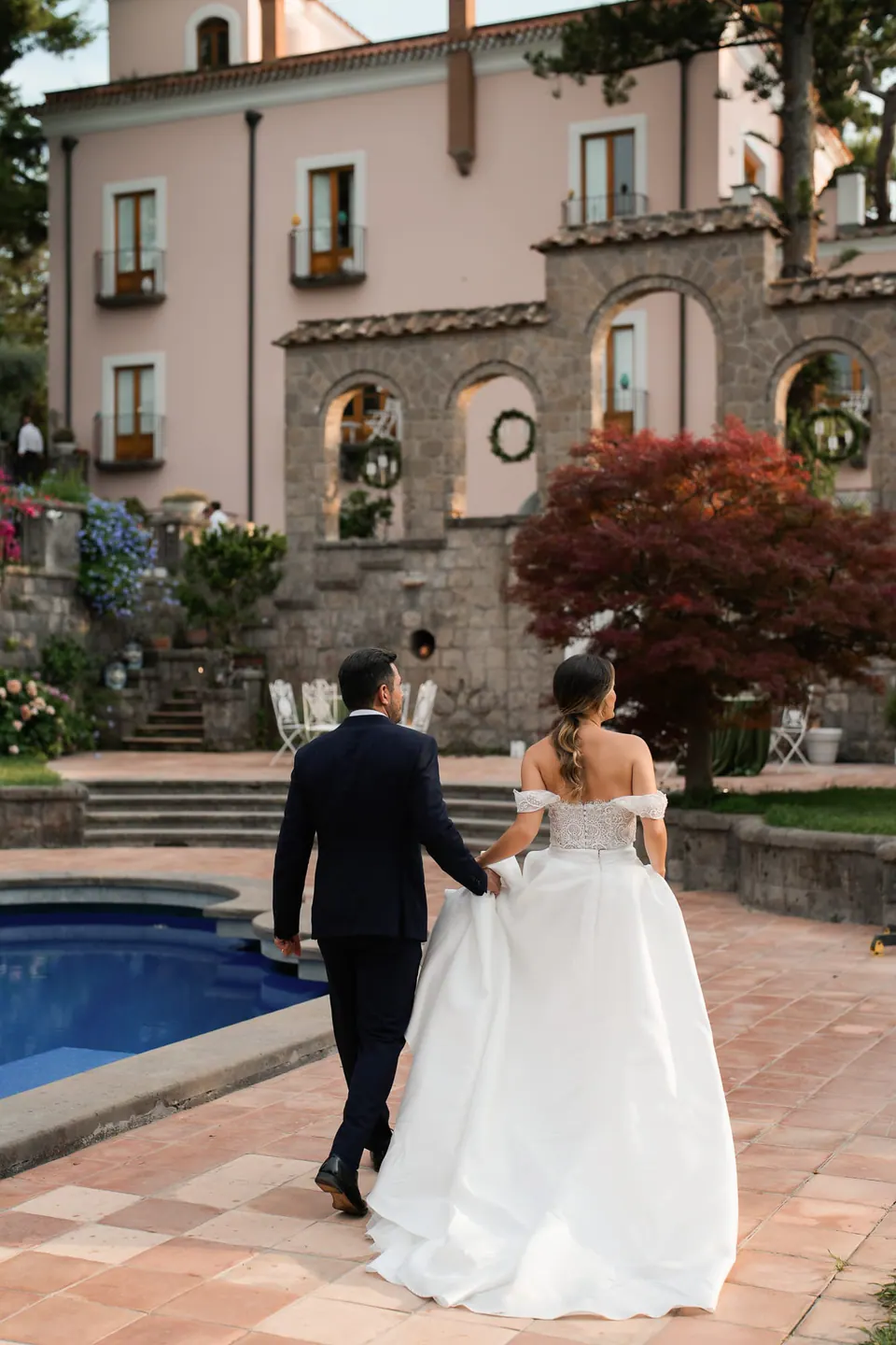 Bride and groom walking by the pool in front of the villa at Capo Santa Fortunata