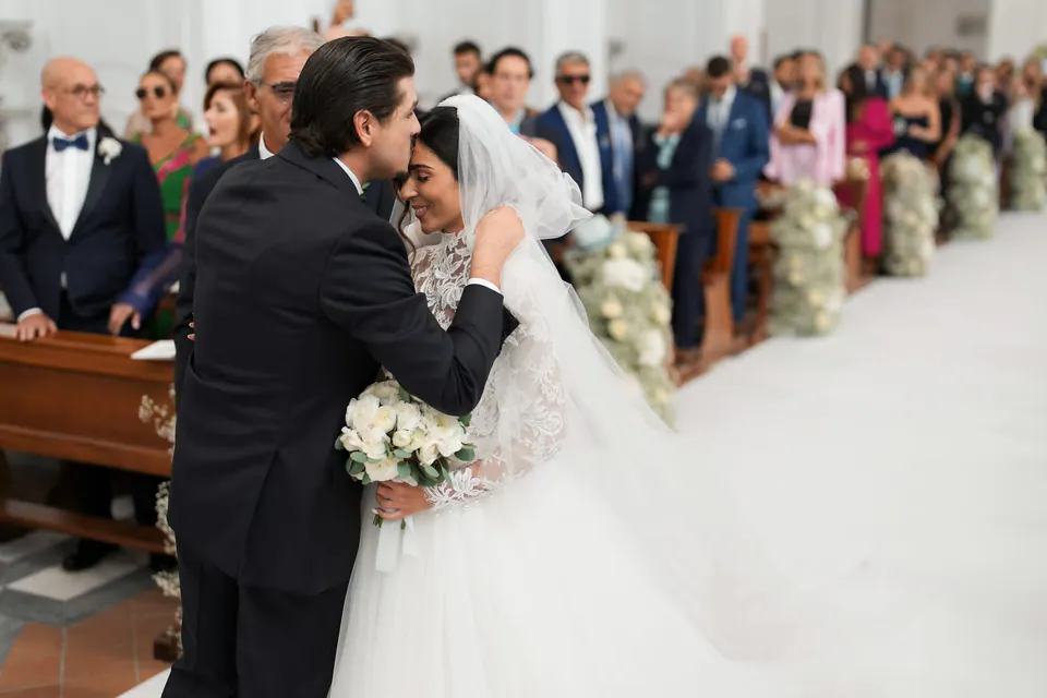 Bride and groom exchanging rings at the altar, with their families around them.
