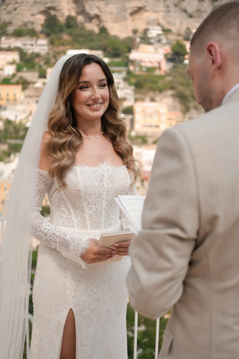 Bride smiling as she reads her vows to the groom on the terrace.