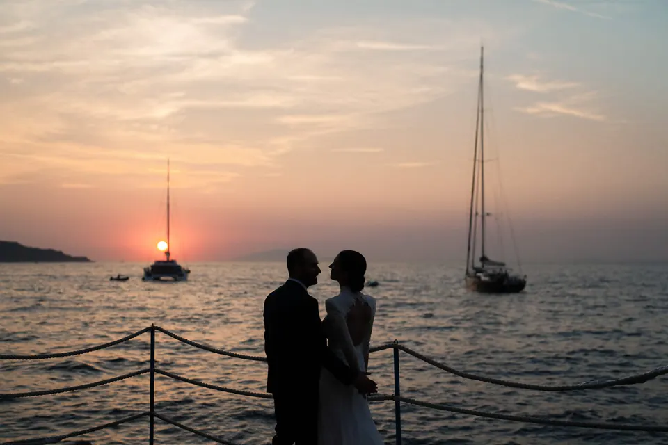 Das Brautpaar als Silhouette vor dem Abendhimmel, dahinter zwei Segelboote.