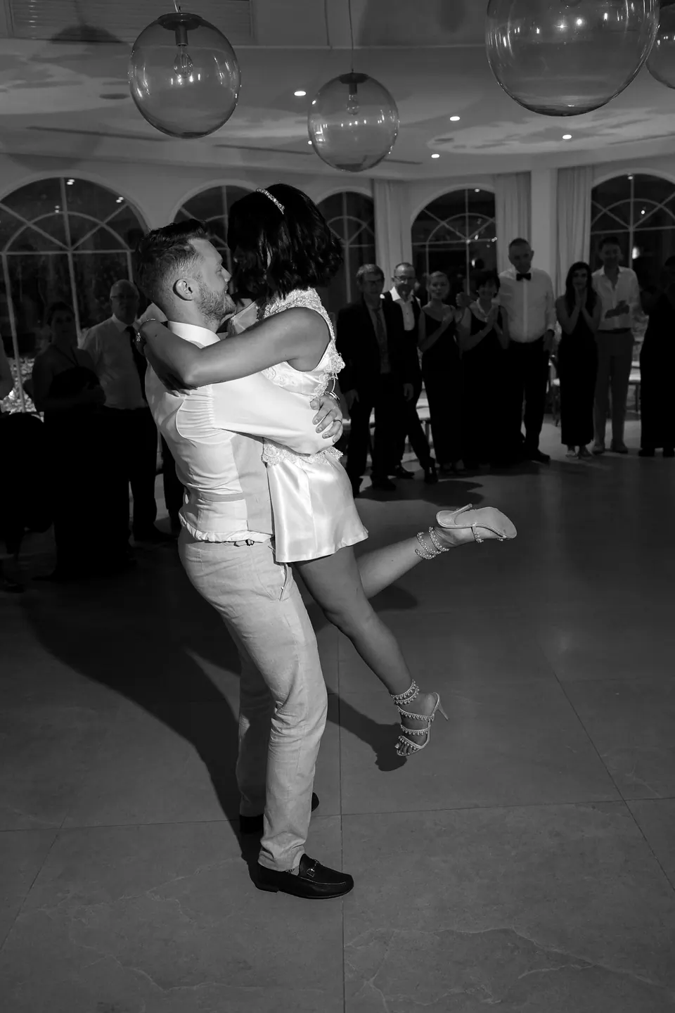 Le marié soulève la mariée dans la salle de réception, en noir et blanc.