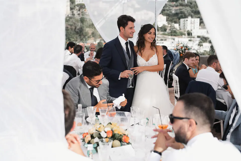 Gli sposi sorridono insieme durante la cena, circondati da familiari e amici nel cortile.