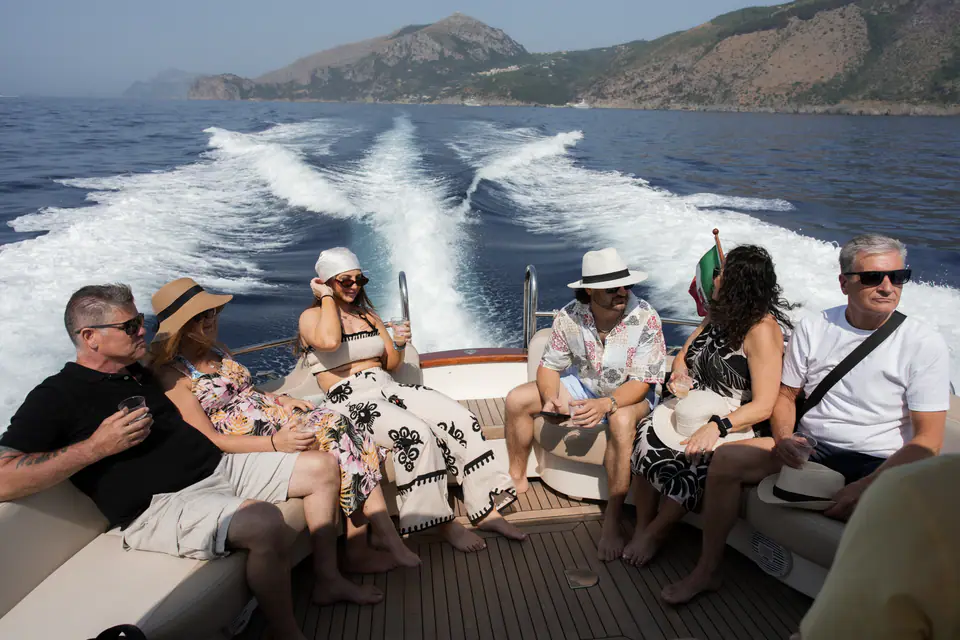 Friends and family on the back of a boat, the wake trailing towards the coast.
