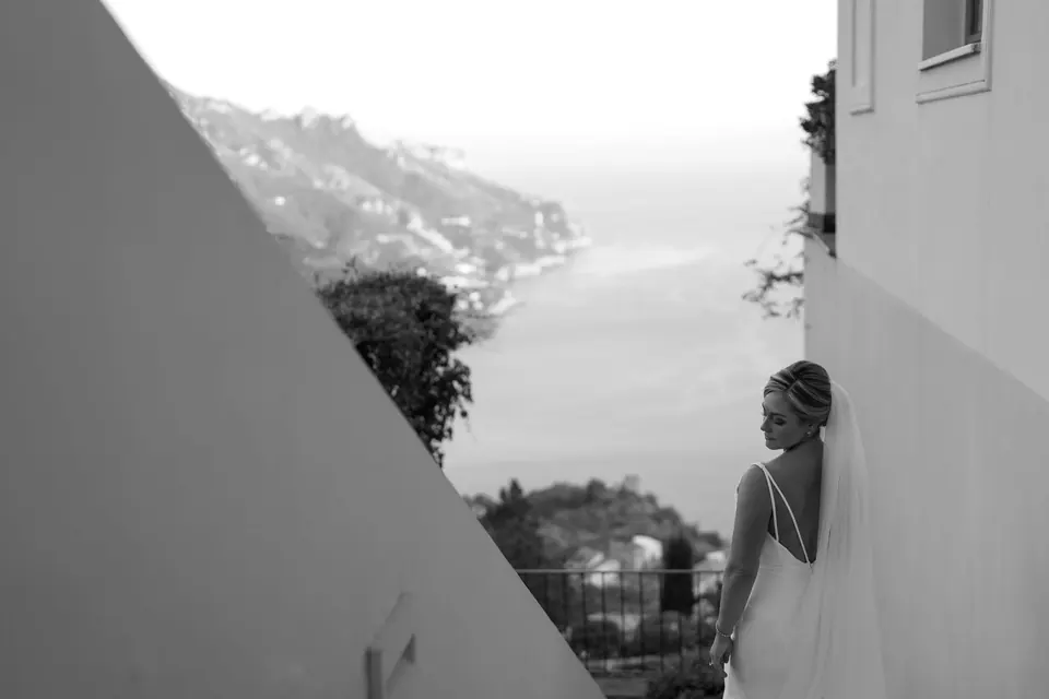 Black and white photo of the bride between white walls, looking out at the coast