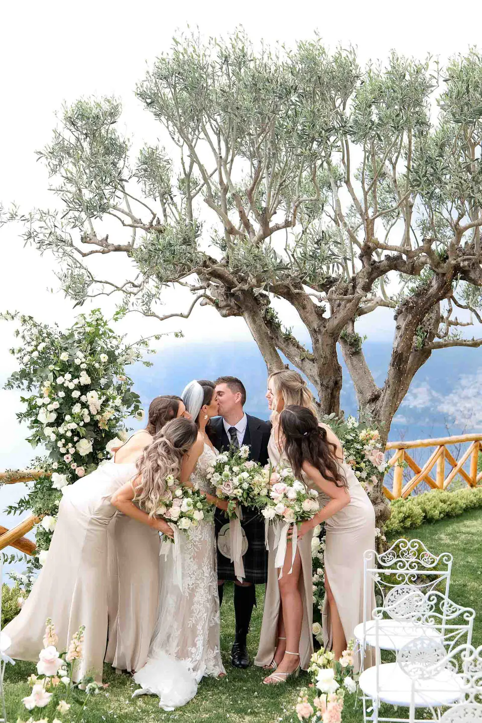La sposa abbraccia le damigelle alla cerimonia in giardino sotto il vecchio ulivo.