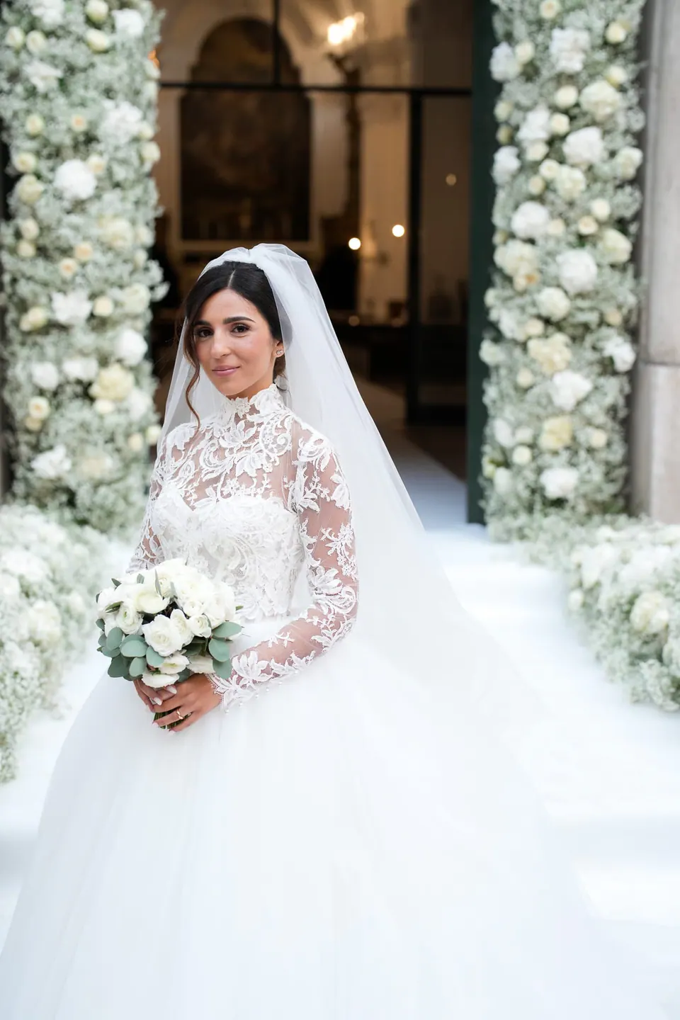 Bride smiling with her bouquet in front of the greenery, afternoon light.