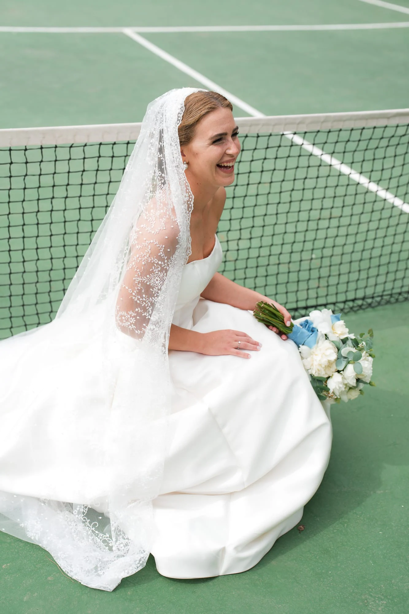 Die Braut lacht, sitzend auf dem grünen Sand des alten Tennisplatzes im La Cocumella.