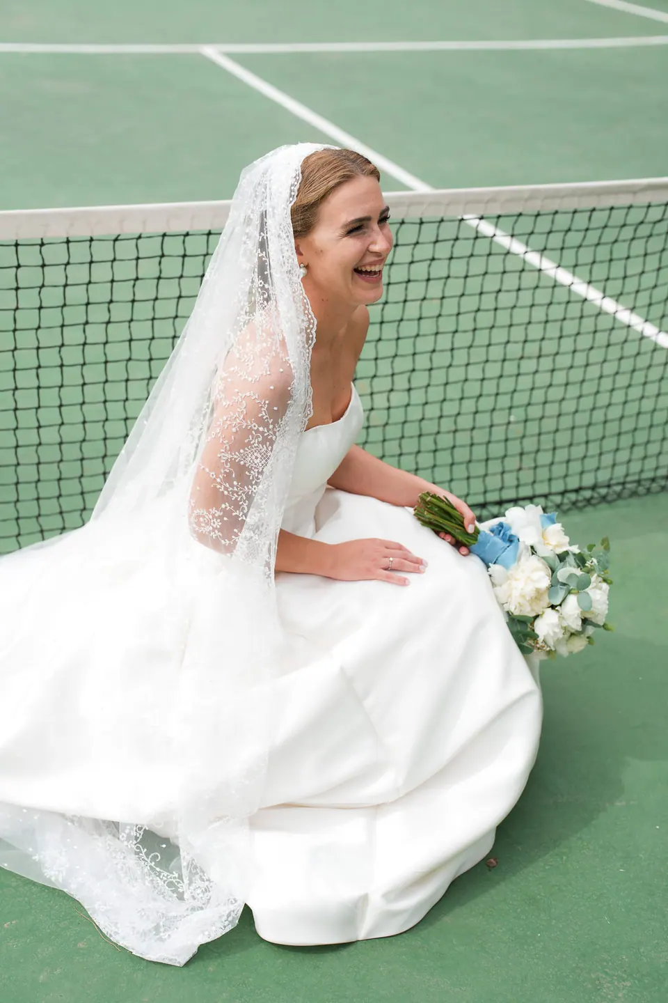 Bride laughing as she sits on the green clay of the old tennis court at La Cocumella.