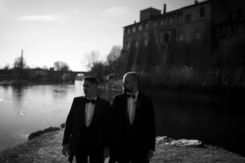 Schwarzweißfoto der Bräutigame am Fluss unter den Burgmauern.