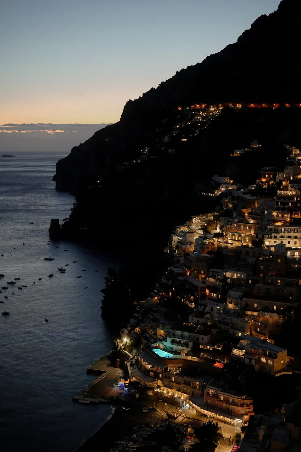 Positano at dusk, the lights of the town coming on above the sea.