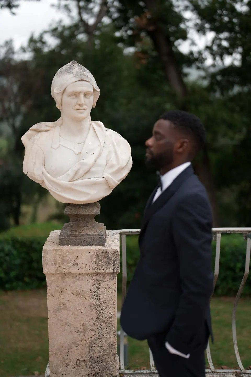 El novio frente a un busto de mármol sobre un pedestal en los jardines de la villa.